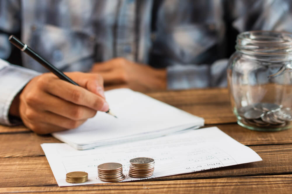 homem escrevendo no papel com moedas na mesa